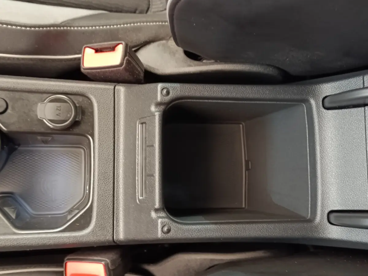 Vue plongeante sur la console centrale noire de la Volkswagen Golf 1.5 eTSI R-Line avec prise 12V et zone de recharge sans fil.