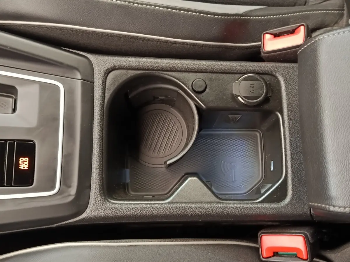 Vue rapprochée de la console centrale noire de la Volkswagen Golf 1.5 eTSI avec zone de recharge sans fil et prise 12V.