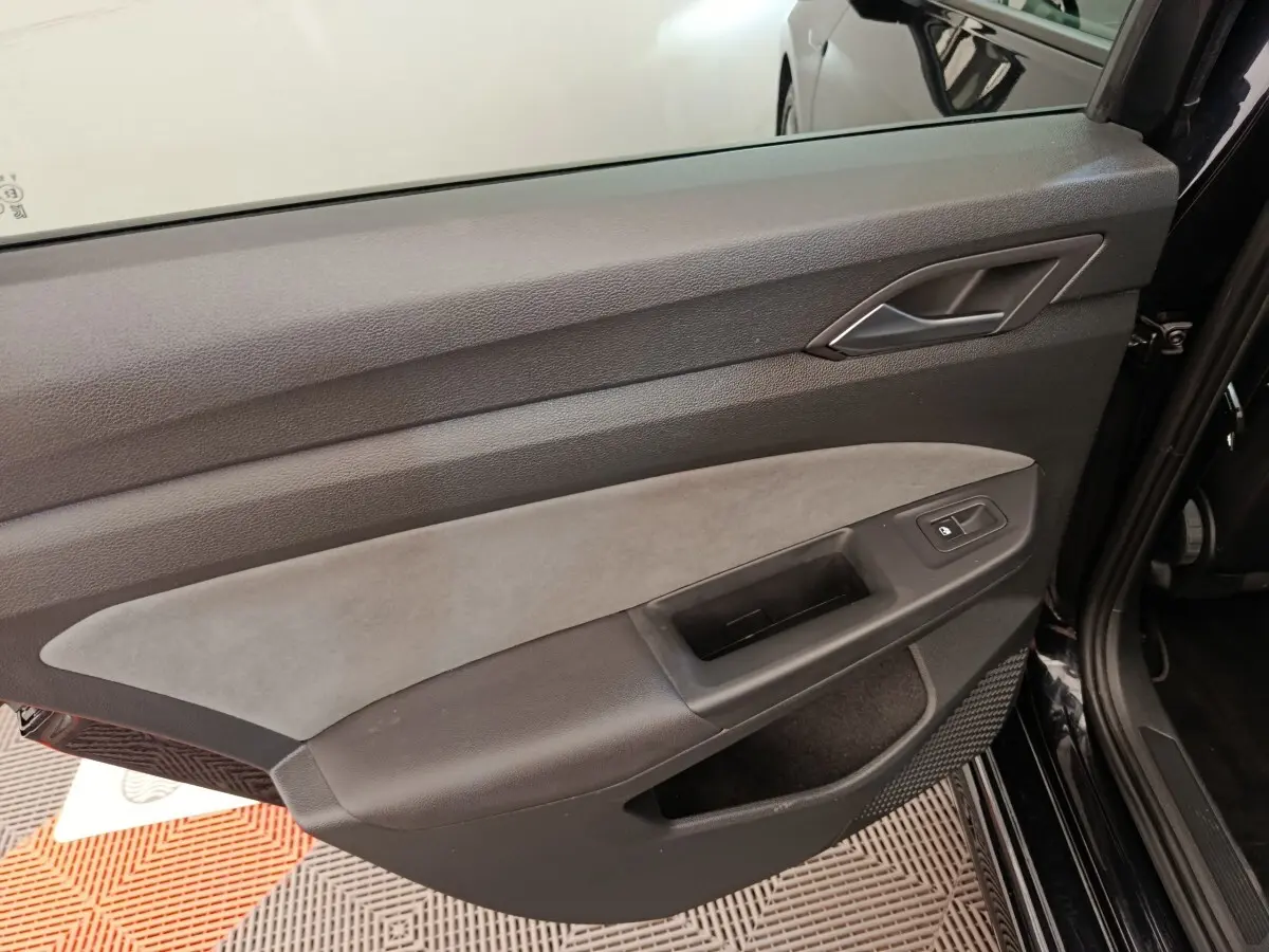 Vue rapprochée de la porte avant droite noire de la Volkswagen Golf 1.5 eTSI avec garniture grise et bouton de verrouillage.