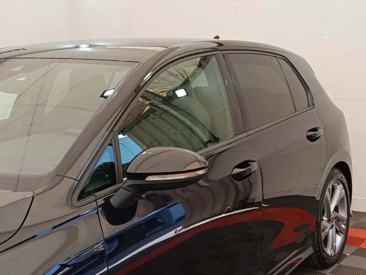 Vue côté gauche avant d'une Volkswagen Golf noire 1.5 eTSI R-Line avec jantes alliage et rétroviseur noir brillant.