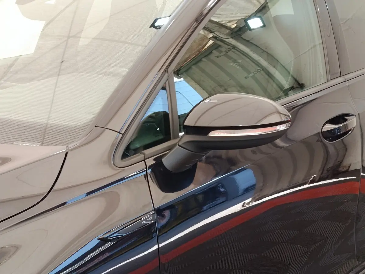 Vue rapprochée du côté gauche d’une Volkswagen Golf noire, mettant en valeur le rétroviseur et la poignée de porte.