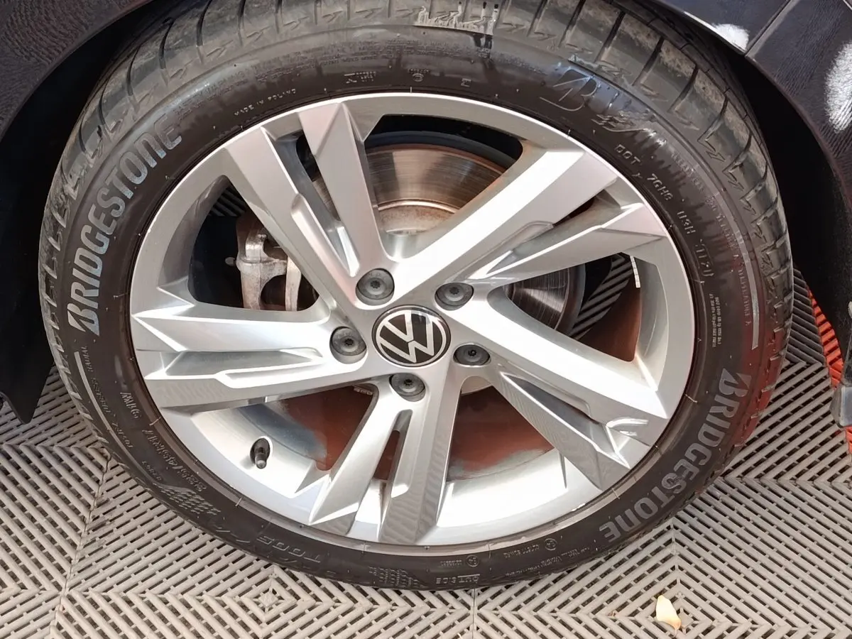 Gros plan sur la jante alliage argentée avec logo Volkswagen au centre d'une Golf noire 1.5 eTSI R-Line.