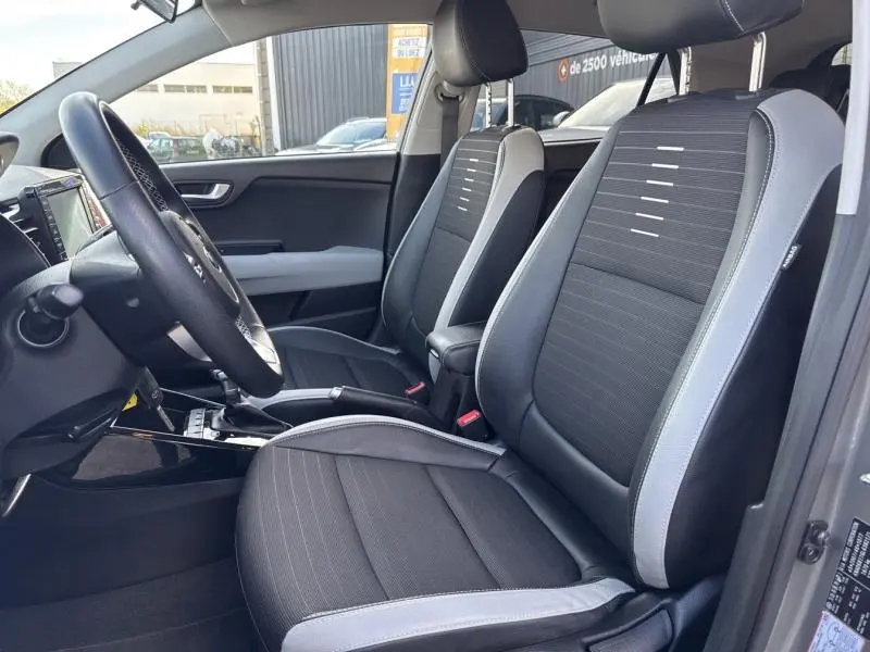 Vue intérieure côté conducteur de la Kia Stonic 2019, sièges tissu noir avec surpiqûres grises et volant cuir.
