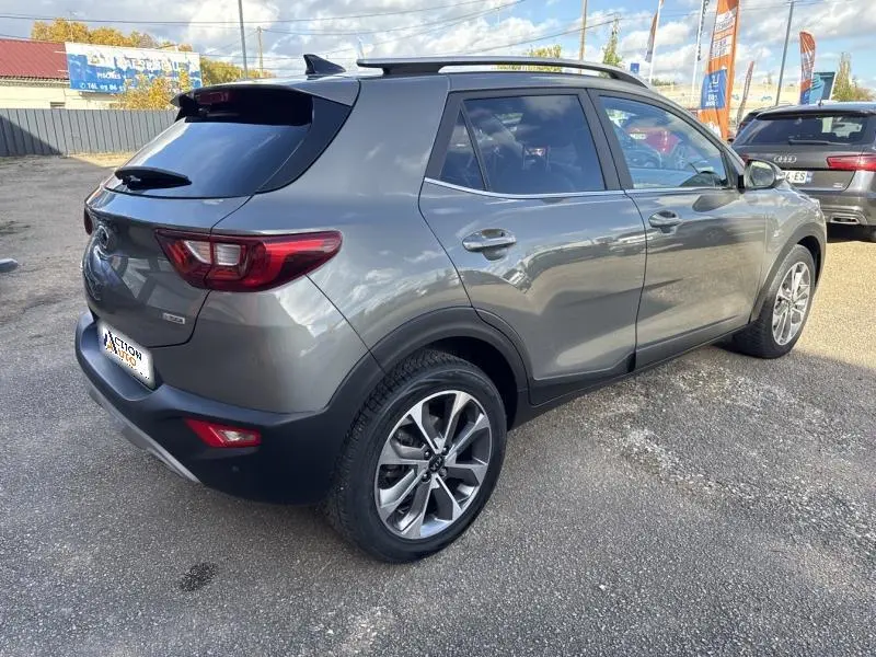 Vue 3/4 arrière droite d'un KIA Stonic brun Sienne avec jantes alliage et barres de toit visibles.