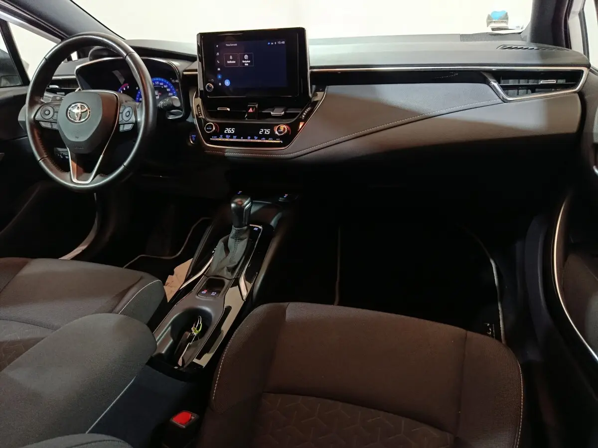 Vue intérieure avant de la Toyota Corolla hybride 2022, tableau de bord noir avec écran tactile central et volant cuir multifonctions.