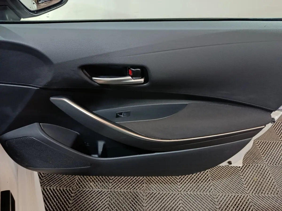 Vue intérieure côté gauche de la porte avant noire de la Toyota Corolla Hybride blanche, avec poignée argentée et haut-parleur intégré.