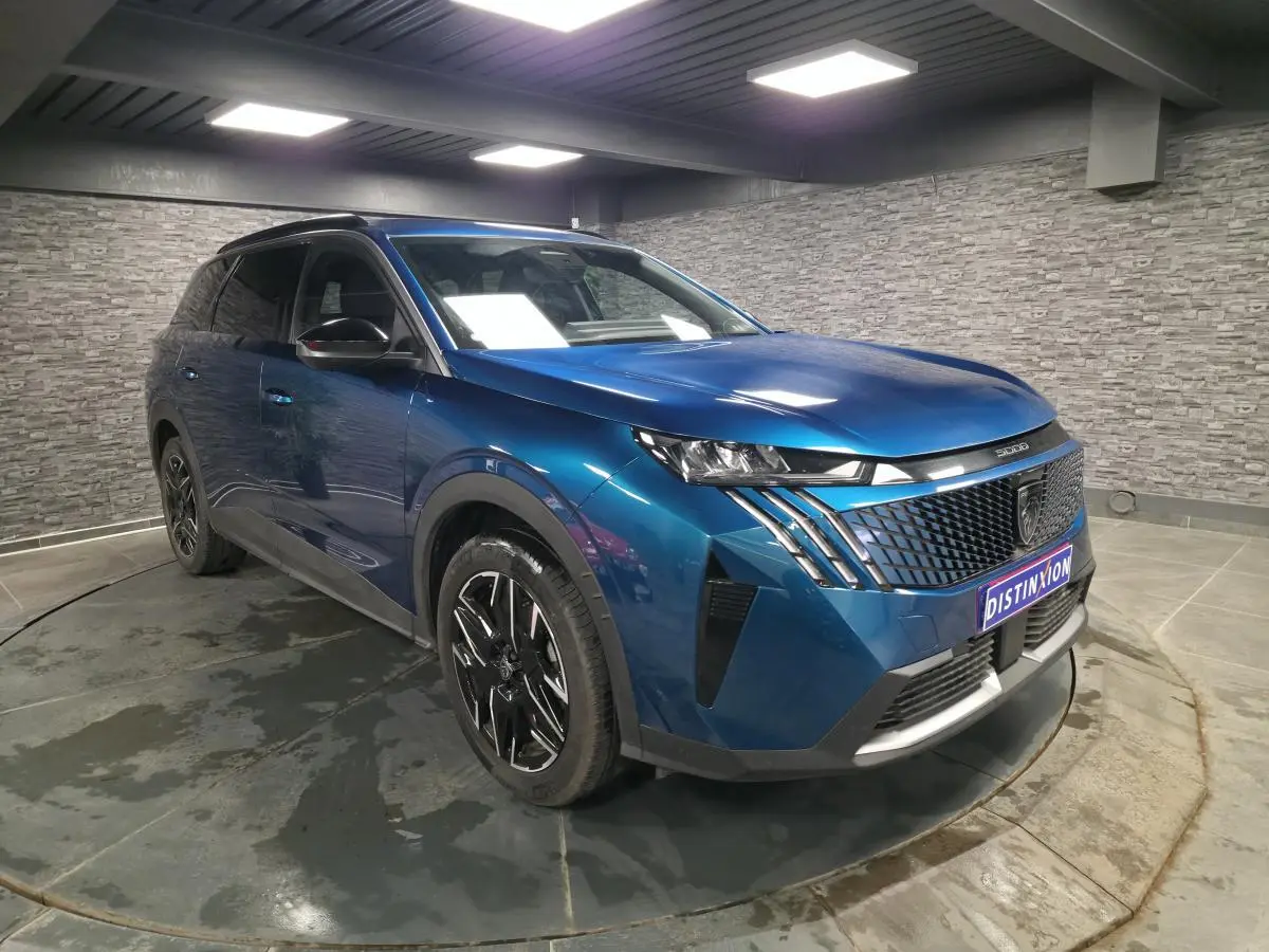 Peugeot 5008 bleu métallisé vue 3/4 avant droit en intérieur avec jantes alliage noires et calandre noire.