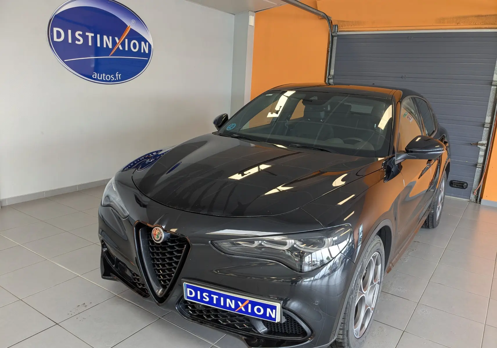 Alfa Romeo Stelvio noir vu en 3/4 avant droit, avec calandre distinctive et jantes alu 19 pouces en showroom.