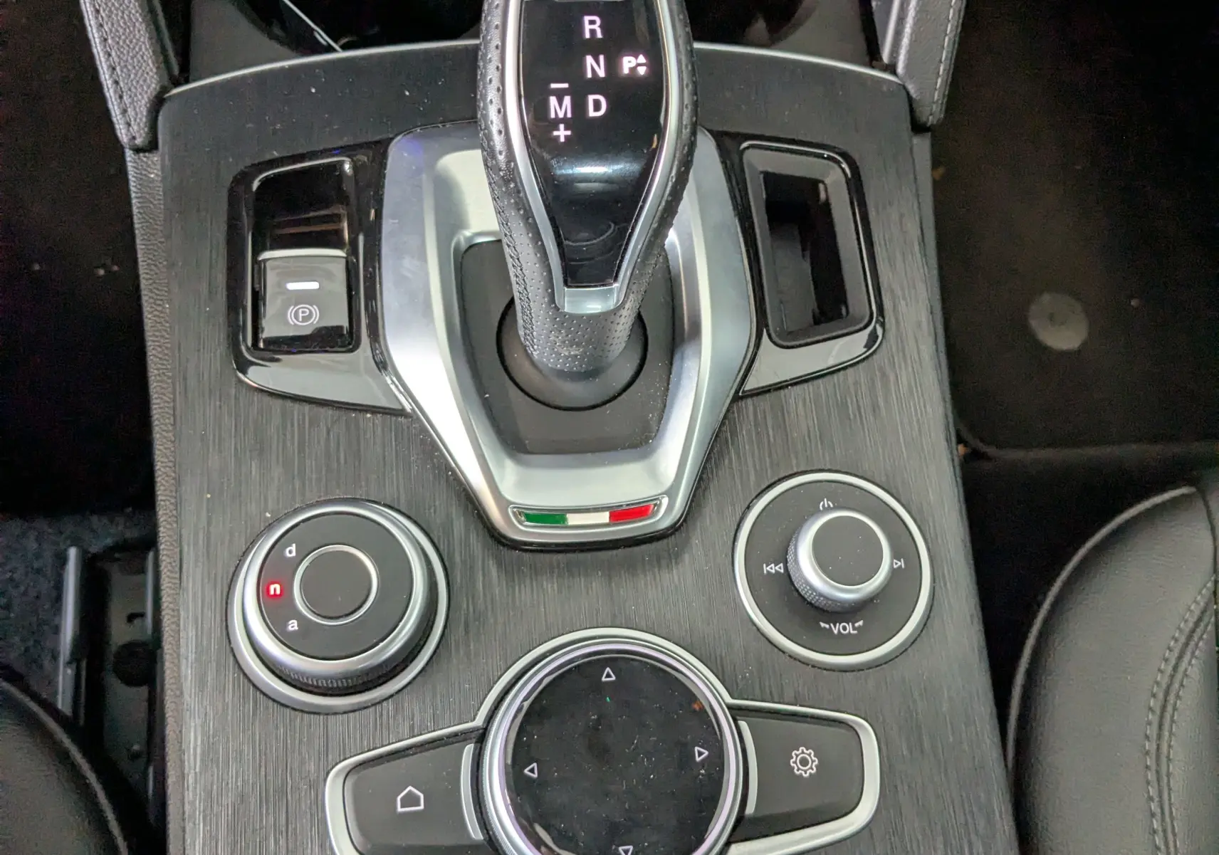 Vue plongeante sur la console centrale noire de l'Alfa Romeo Stelvio 2023, mettant en valeur le levier de vitesses automatique et les commandes multimédia.