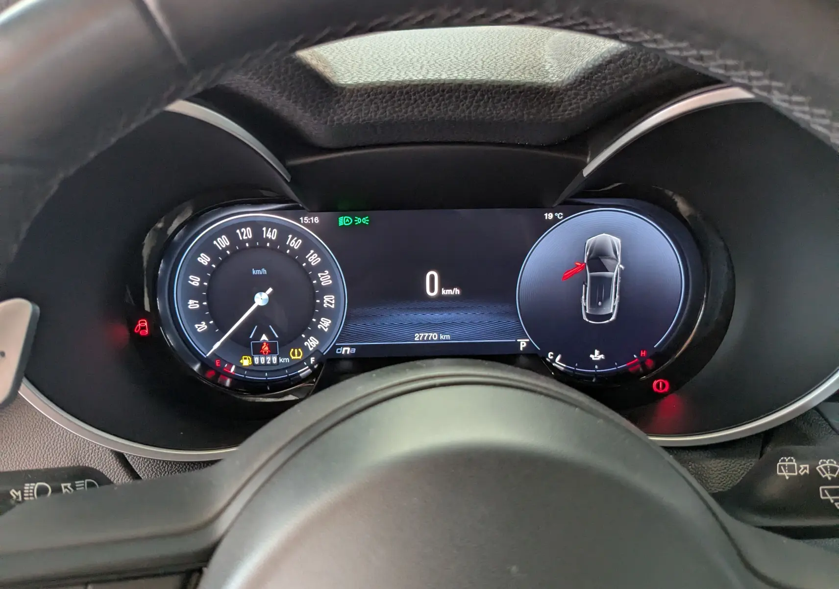 Vue rapprochée du tableau de bord numérique de l'Alfa Romeo Stelvio noir, affichant la vitesse et l'alerte porte ouverte côté gauche.