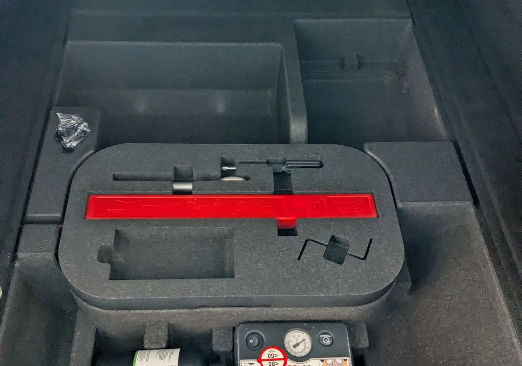 Compartiment de rangement sous le hayon de l'Alfa Romeo Stelvio noir 2023, montrant kit de réparation pneus et espace vide.