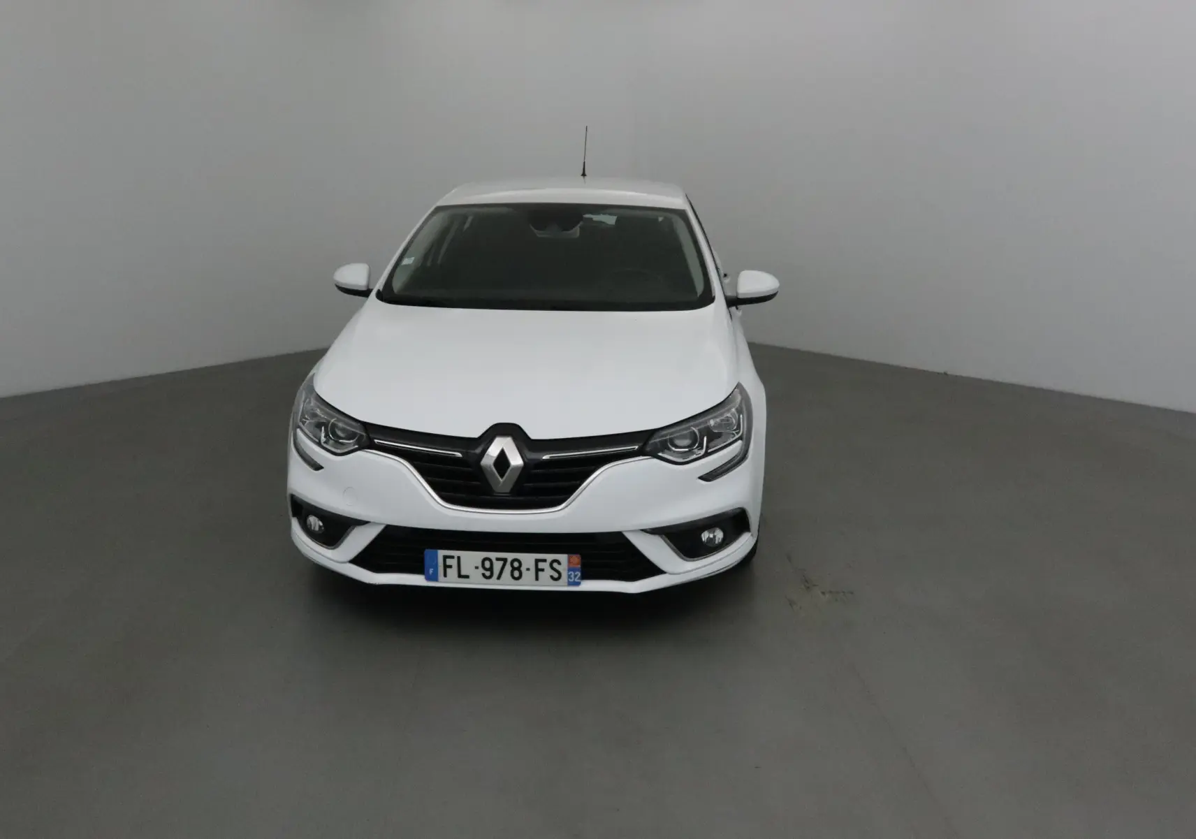 Vue frontale d'une Renault Mégane IV Berline blanche avec logo Renault bien visible sur calandre noire.