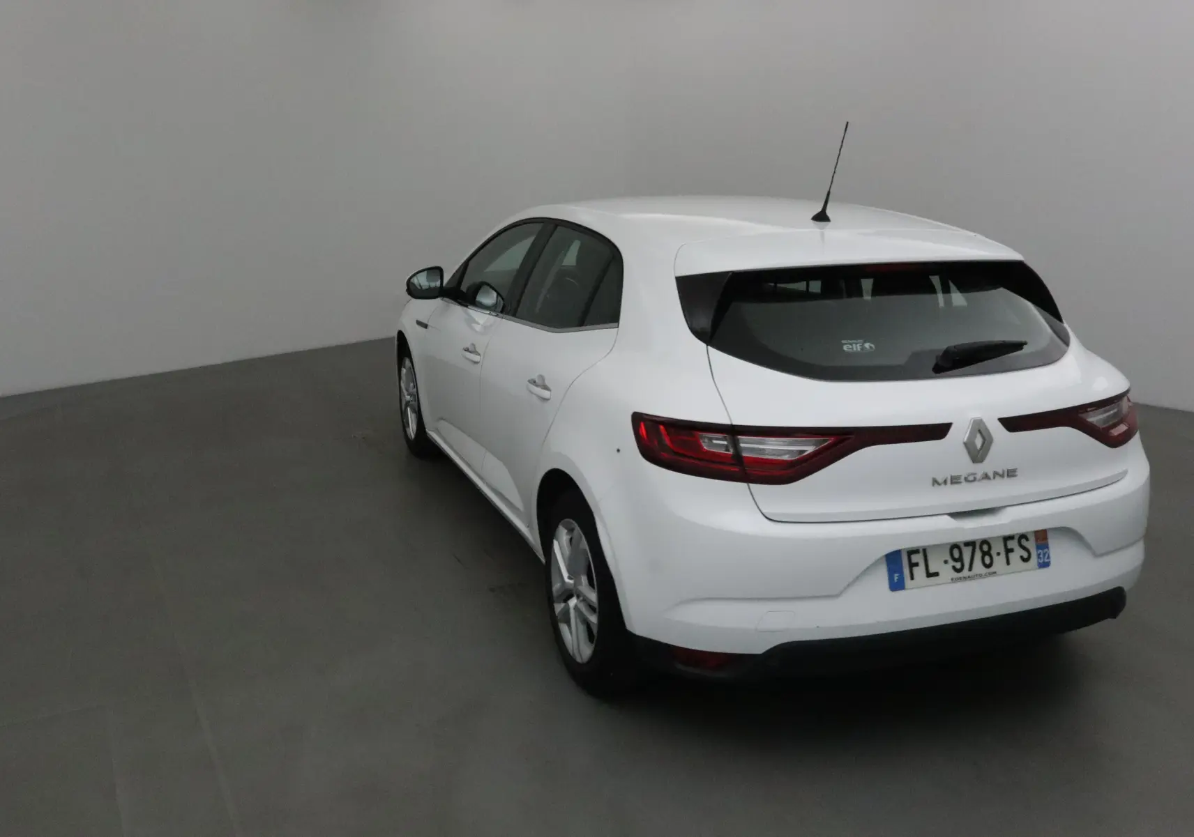 Vue 3/4 arrière droite d'une Renault Mégane IV berline blanche avec feux arrière allongés et antenne de toit.