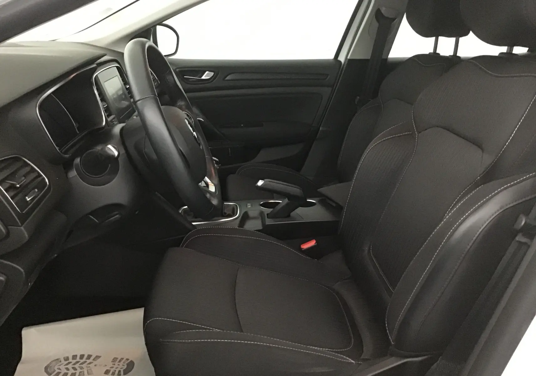 Intérieur côté conducteur de la Renault Mégane IV Berline blanche, montrant sièges noirs et tableau de bord avec volant multifonction.