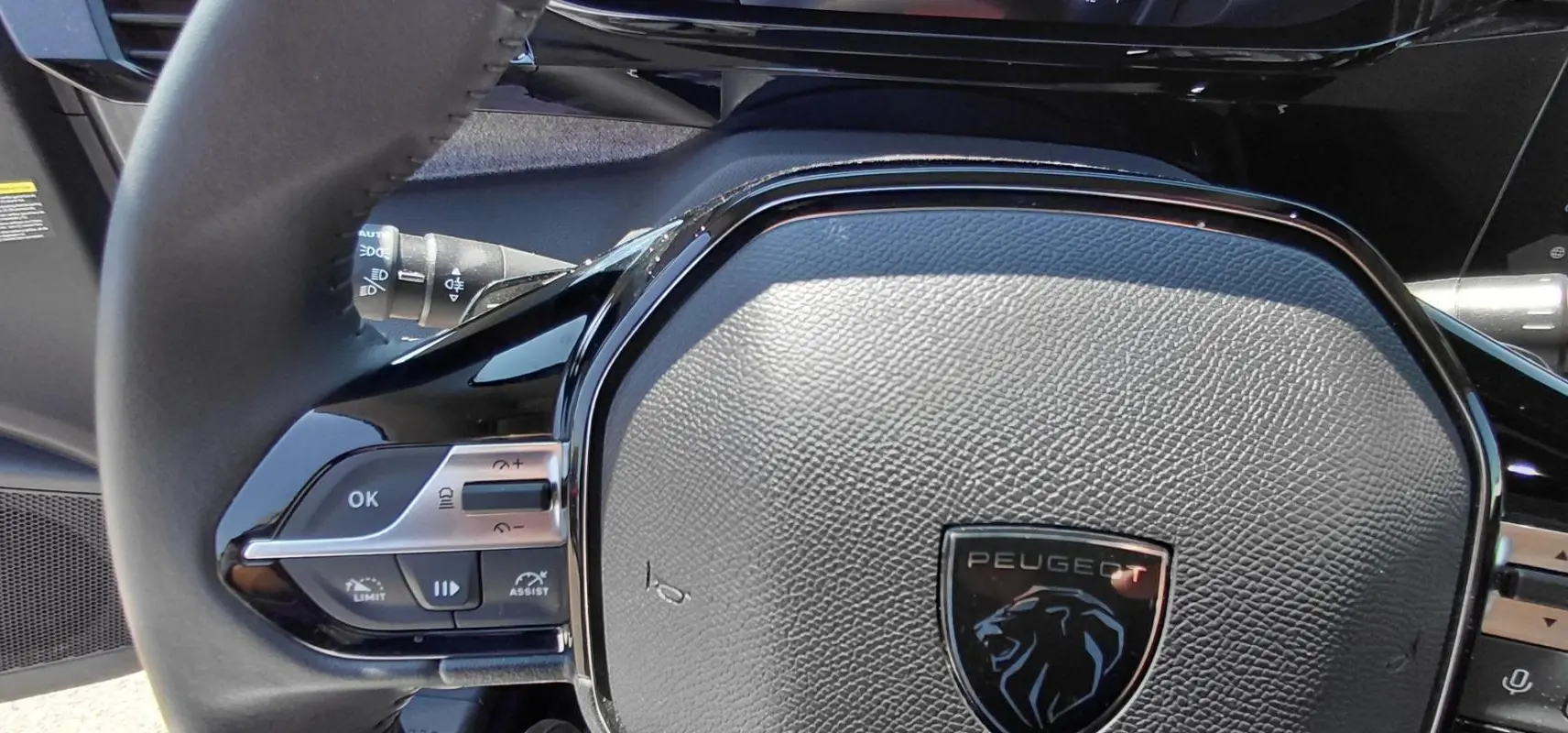 Gros plan sur le volant noir texturé du Peugeot 308 SW Hybrid 145 Allure avec commandes intégrées et logo lion.