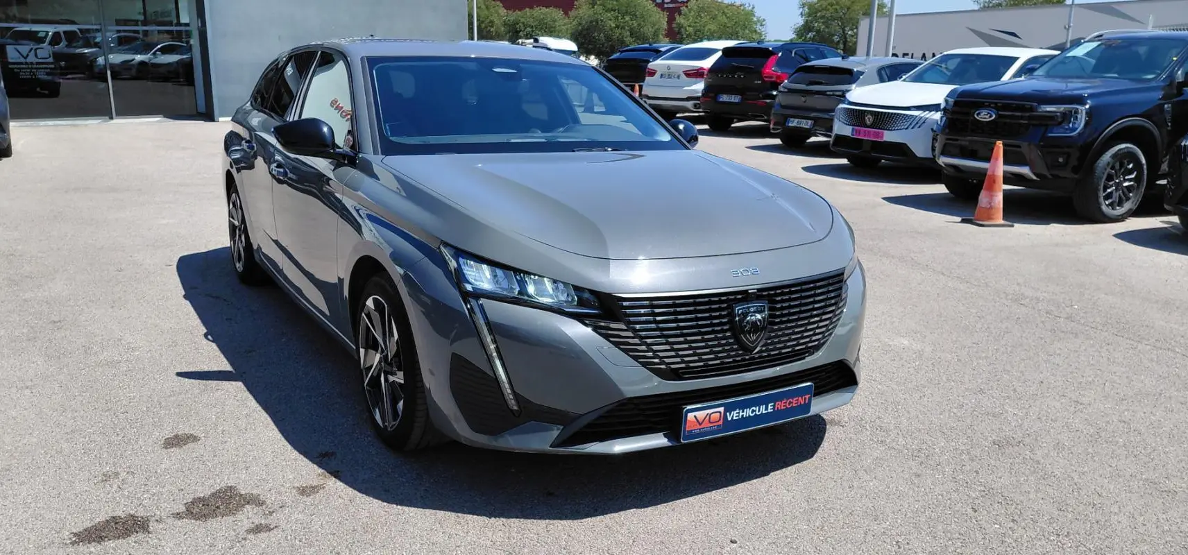 Peugeot 308 SW gris vue 3/4 avant droit, avec calandre noire distinctive et jantes alliage 17 pouces.