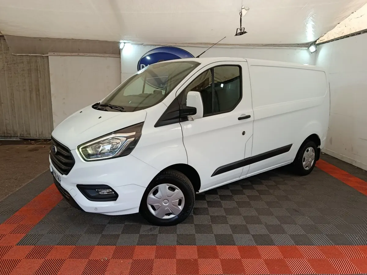 Vue 3/4 avant droit d'un fourgon Ford Transit Custom blanc avec calandre noire et feux avant allumés.