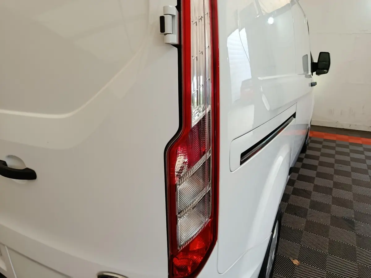 Vue arrière côté droit du fourgon blanc Ford Transit Custom avec feu arrière vertical et poignée de porte visible.