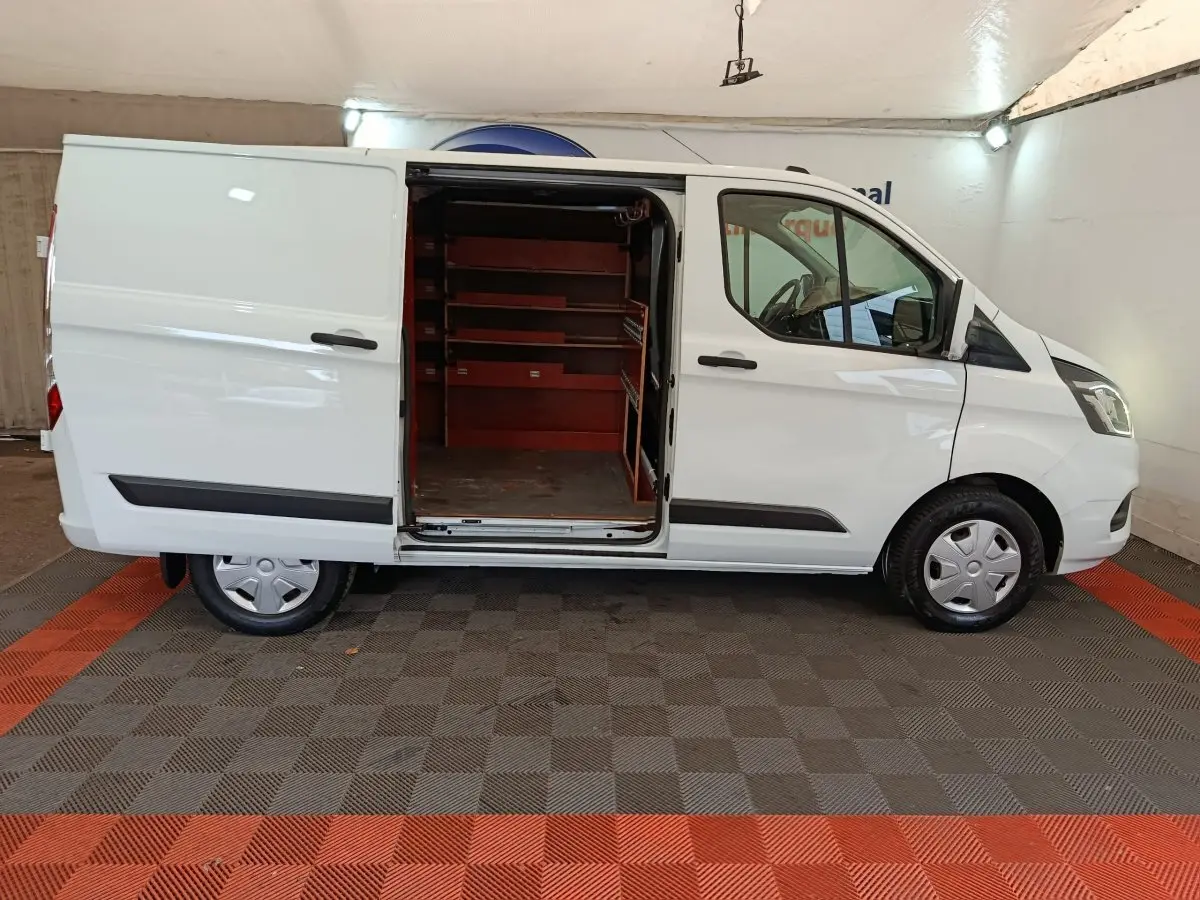 Vue latérale droite d'un Ford Transit Custom blanc 2020 avec porte coulissante ouverte révélant l'intérieur aménagé en étagères rouges.