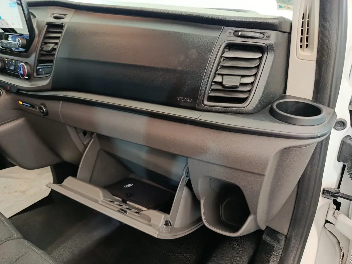 Vue intérieure côté passager du tableau de bord gris et noir du Ford Transit Custom avec boîte à gants ouverte et porte-gobelet.
