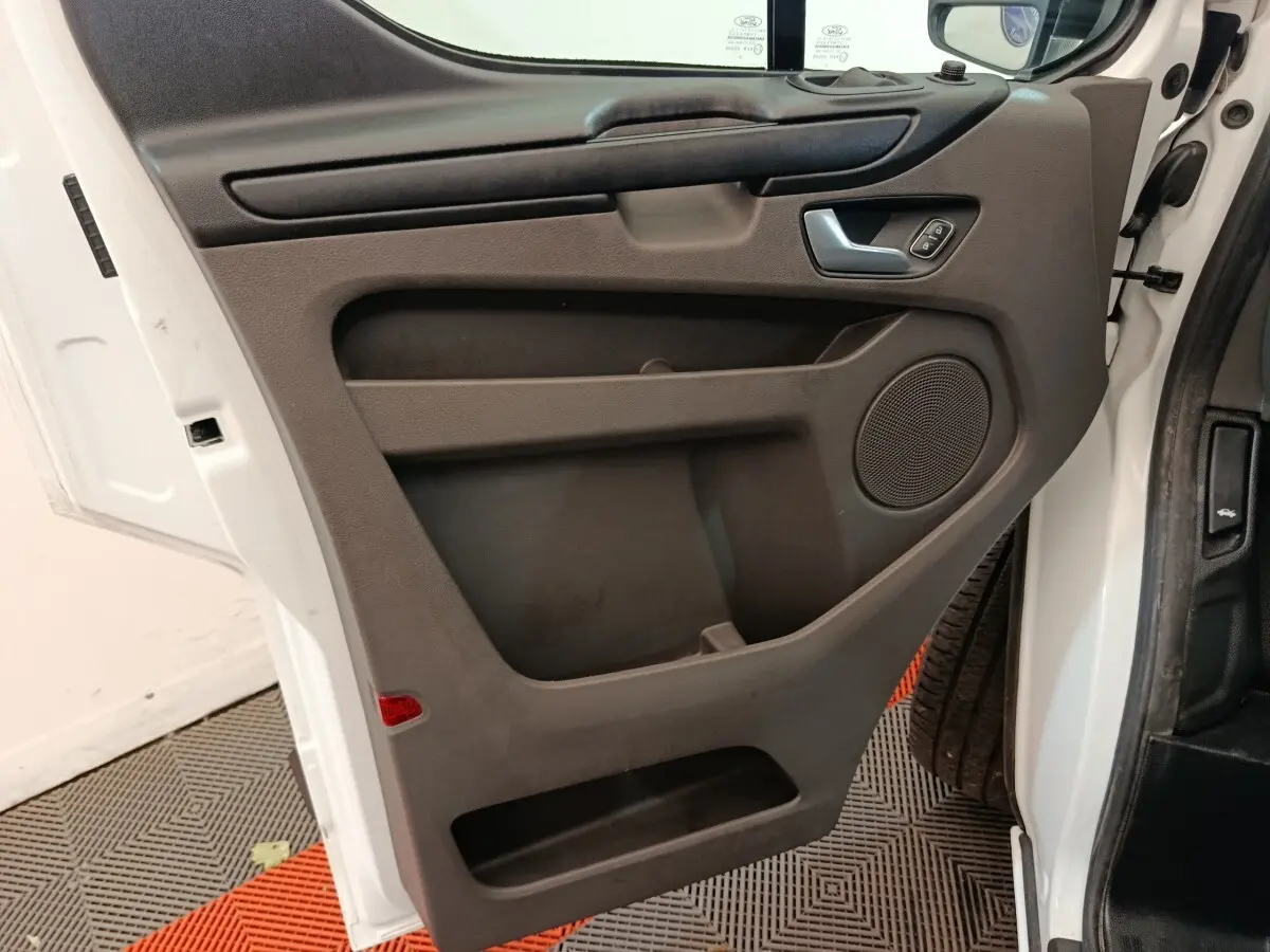 Vue intérieure côté gauche de la porte avant blanche du Ford Transit Custom avec panneau noir et haut-parleur intégré.