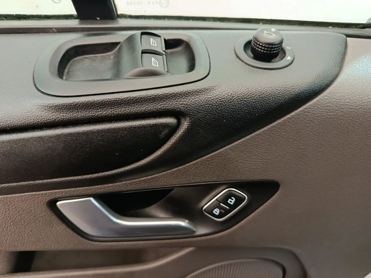 Gros plan sur la porte côté conducteur du Ford Transit Custom blanc, montrant les commandes des vitres et la poignée argentée.