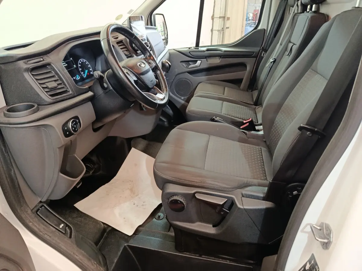 Vue intérieure côté conducteur du Ford Transit Custom blanc 2020, montrant le tableau de bord et la banquette avant grise.