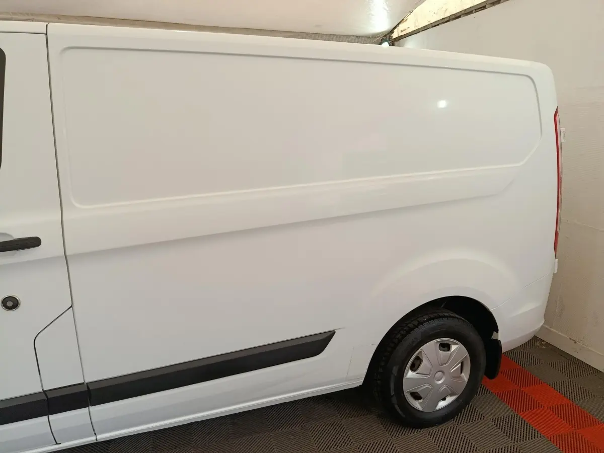 Vue latérale côté droit d'un fourgon Ford Transit Custom blanc, avec porte latérale pleine et jante acier.