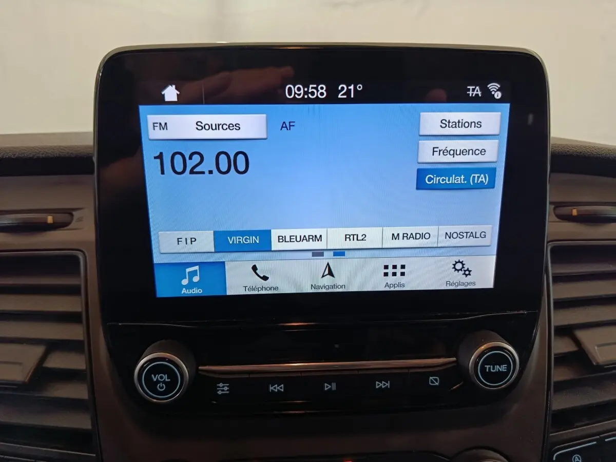 Écran tactile central du Ford Transit Custom blanc, affichant la radio FM à 102.00 MHz en intérieur véhicule.