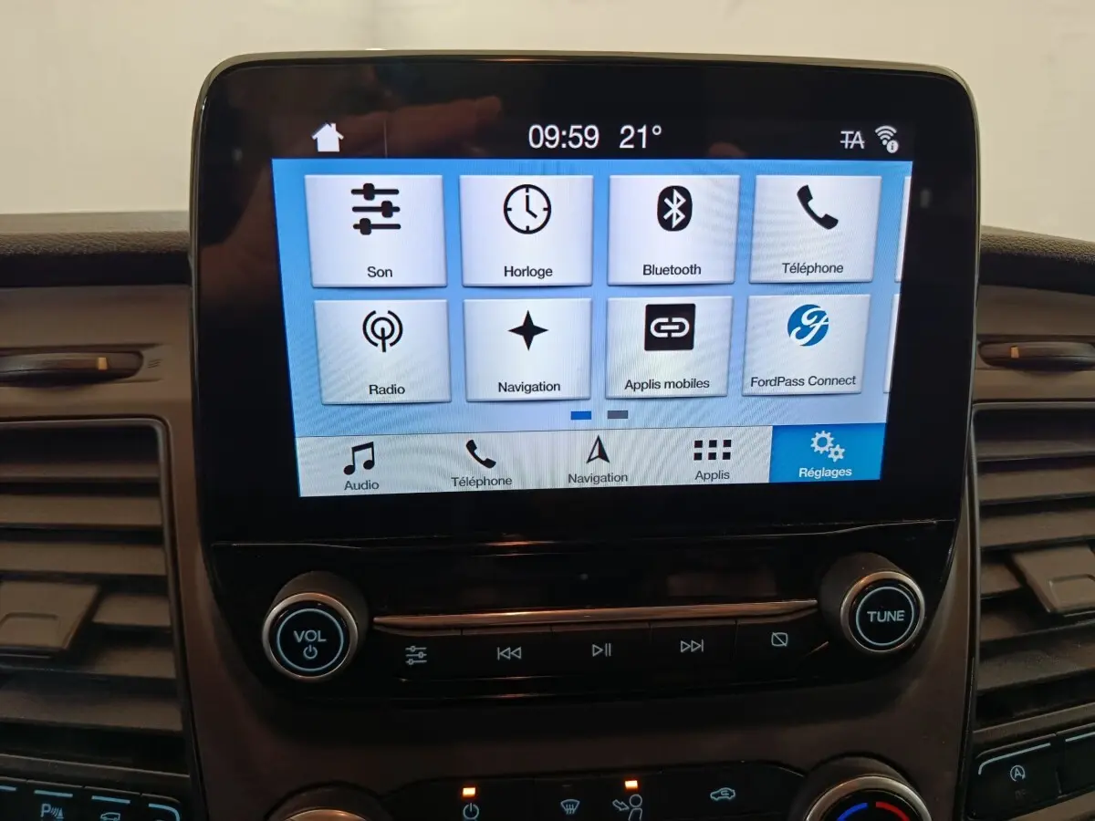 Écran tactile central du Ford Transit Custom blanc, affichant les options multimédia et réglages, vue intérieure frontale.