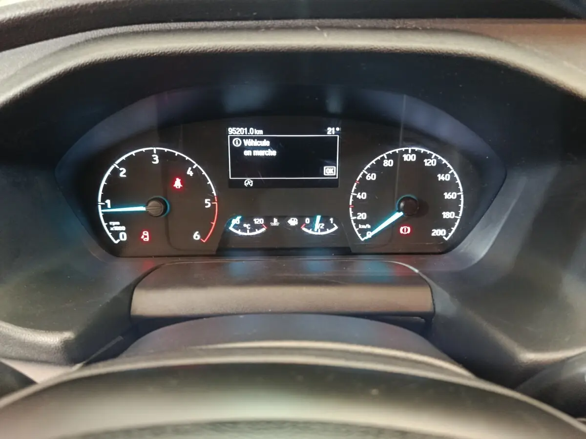 Vue rapprochée du tableau de bord numérique du Ford Transit Custom blanc, affichant 95 201 km et alertes actives.
