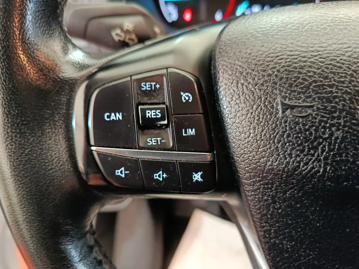 Gros plan sur les commandes de régulateur de vitesse et volume au volant cuir noir du Ford Transit Custom Fourgon blanc.