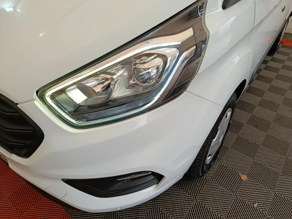 Gros plan sur le phare avant droit du Ford Transit Custom blanc, avec partie de la roue et pare-chocs visibles.