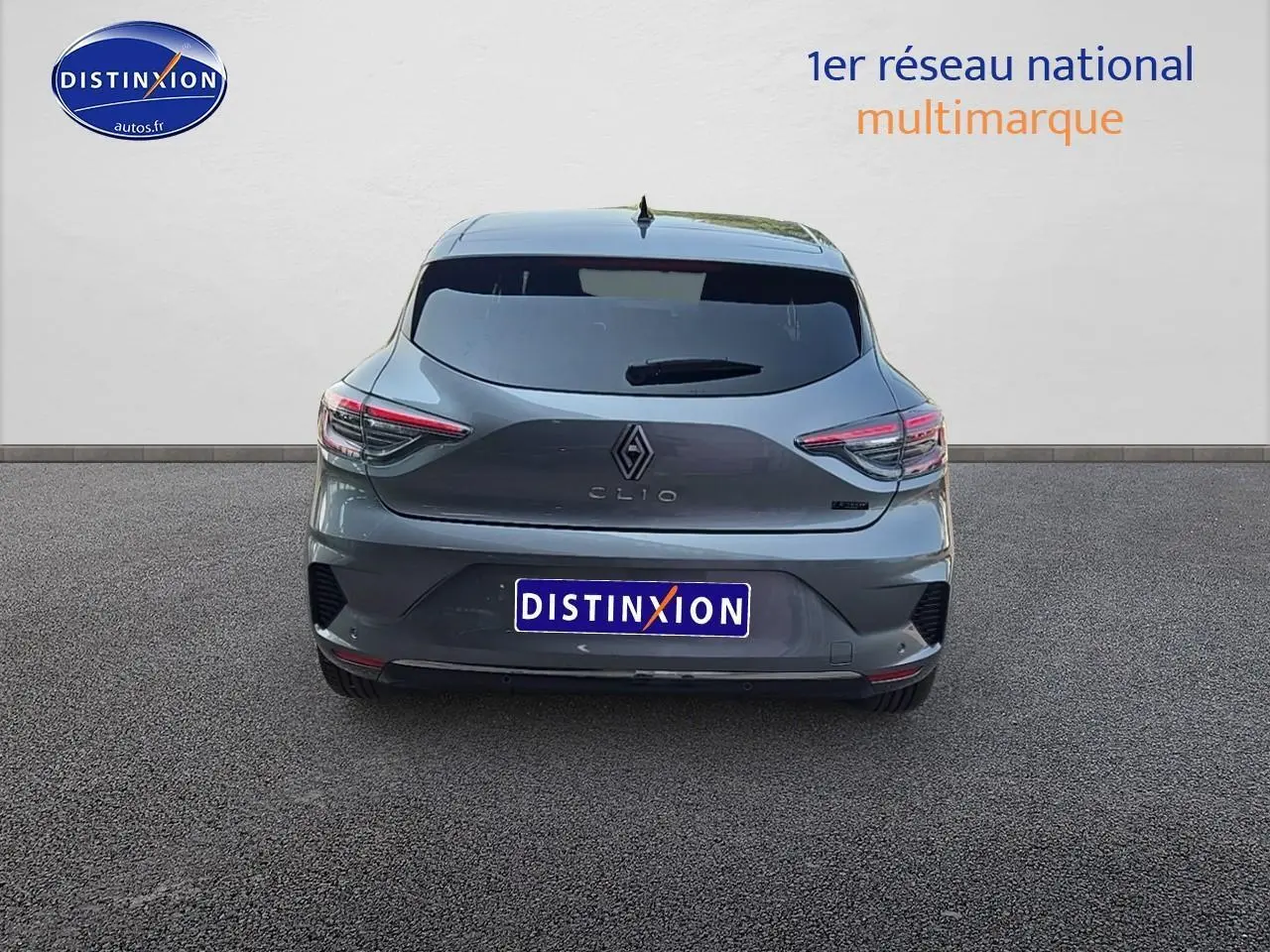 Vue arrière d'une Renault Clio V gris schiste avec feux LED et becquet arrière, stationnée sur sol gris.
