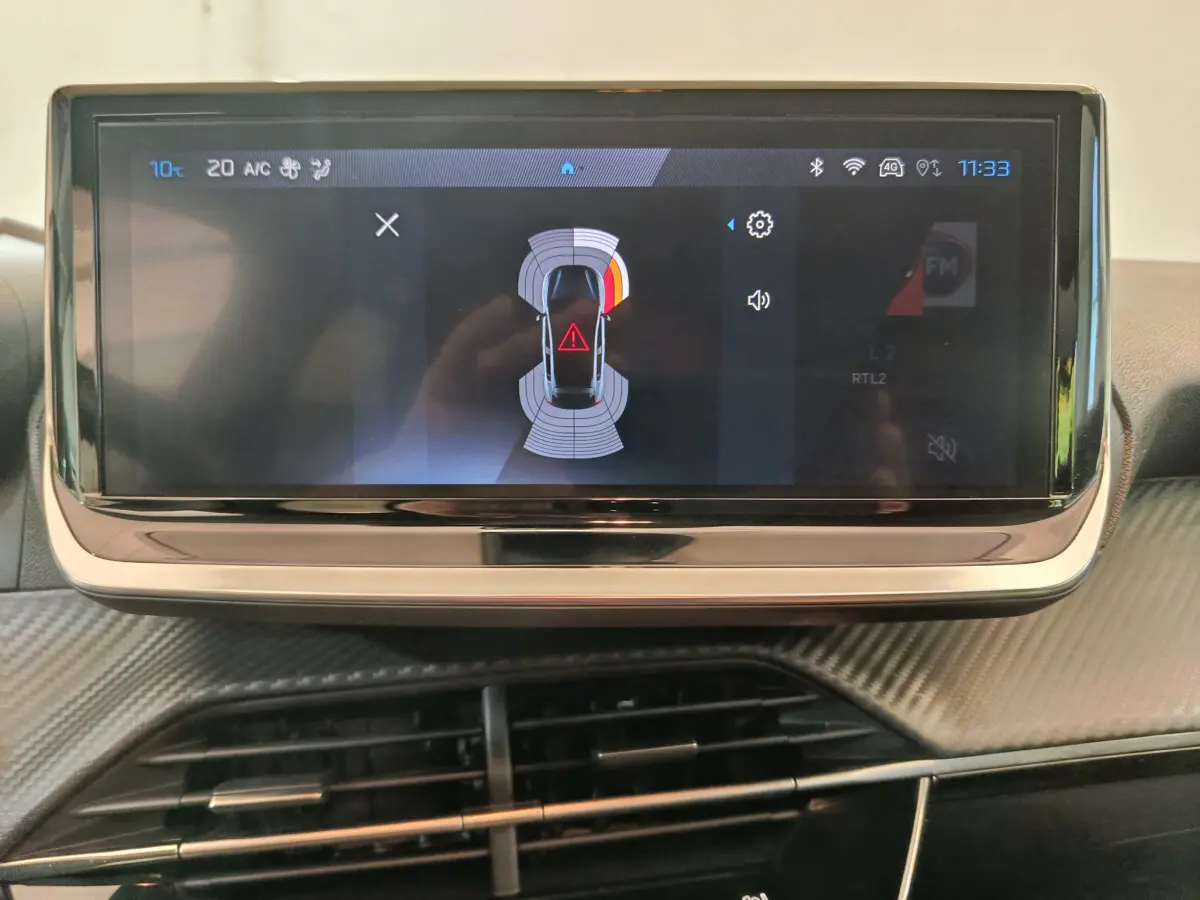 Écran tactile central de la Peugeot 208 PureTech 100 Allure 2025 affichant l'aide au stationnement en intérieur.