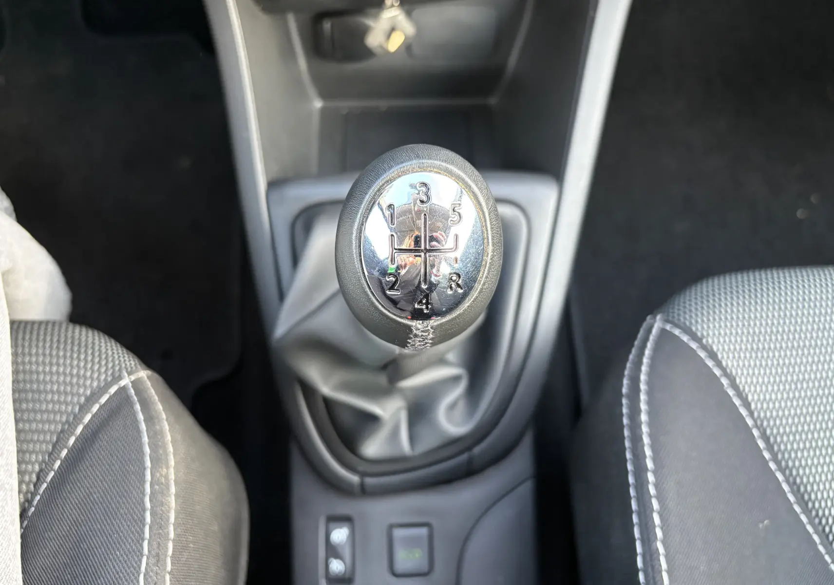 Gros plan sur le levier de vitesses manuel de la Renault Clio IV gris, entouré des sièges avant en tissu gris.