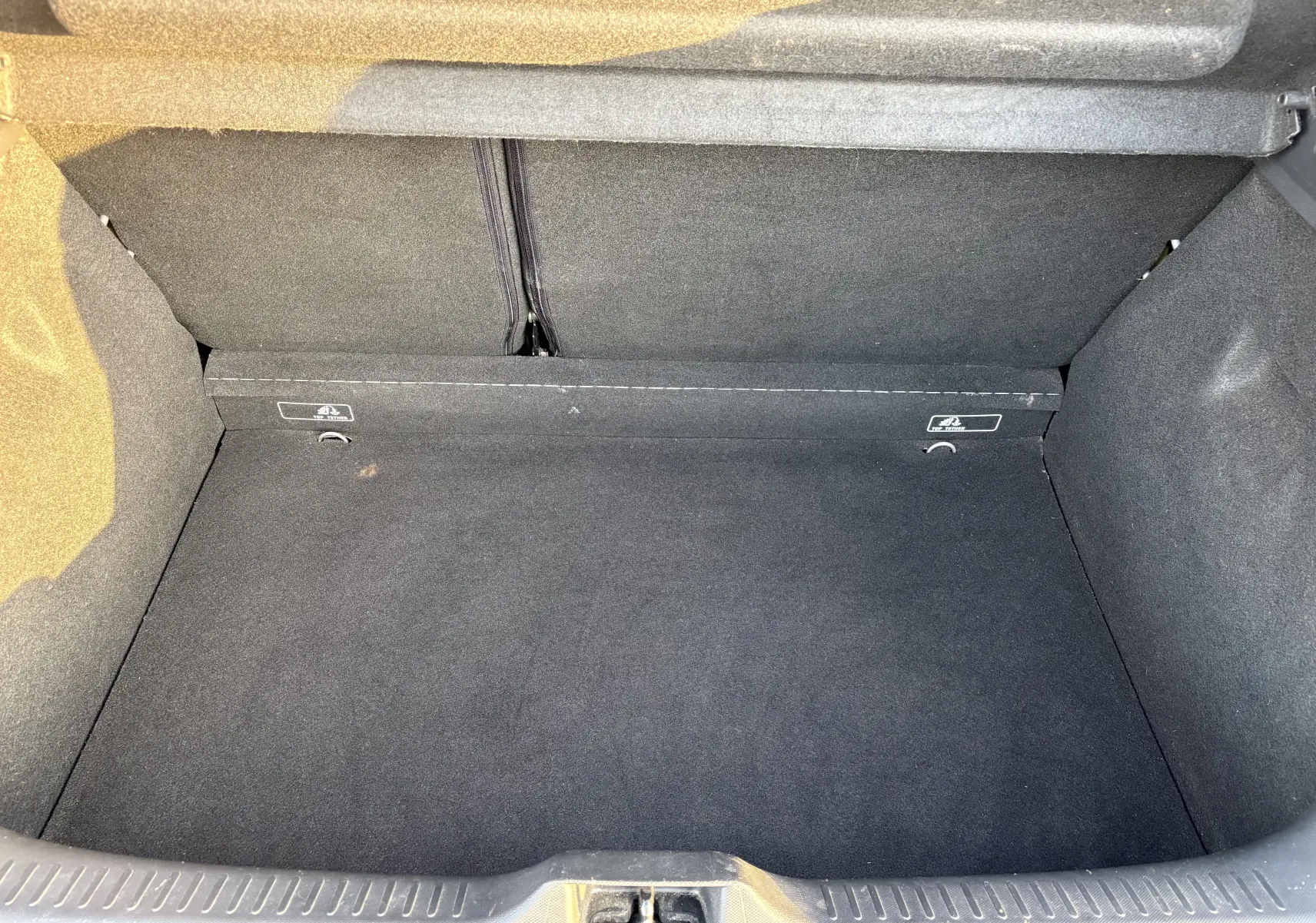 Coffre vide vu de face d’une Renault Clio IV gris, montrant la moquette noire et les fixations arrière.