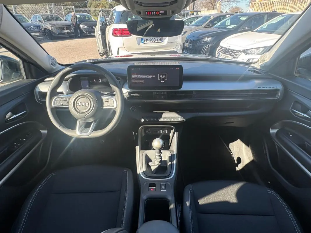 Vue intérieure avant du Jeep Avenger gris 2025, avec tableau de bord moderne et levier de vitesse manuel.