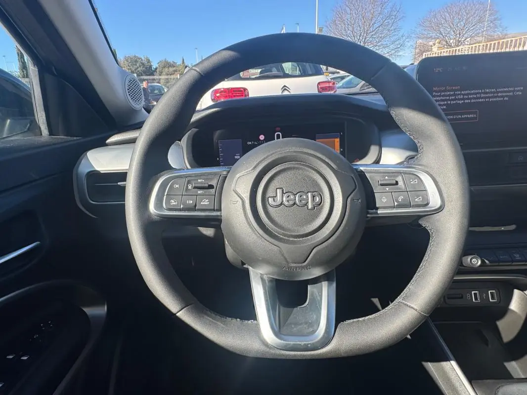 Vue intérieure centrée sur le volant noir du Jeep Avenger 2025, avec tableau de bord et écran digital en arrière-plan.