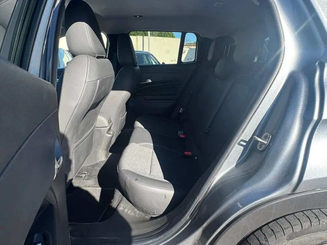 Vue intérieure arrière côté gauche du Jeep Avenger gris 2025, montrant les sièges arrière et la portière ouverte.