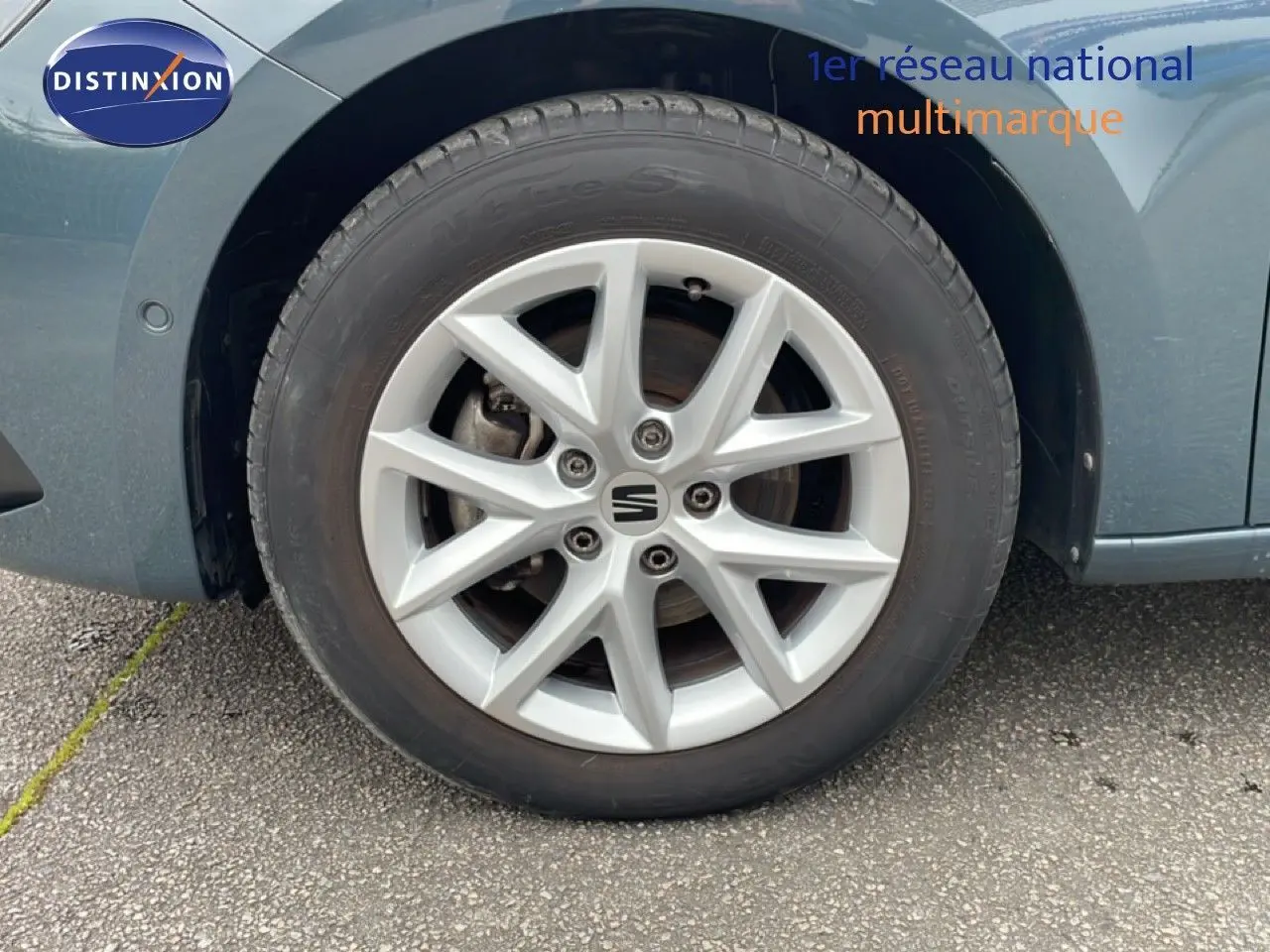 Gros plan sur la roue avant droite d'une SEAT LEON ST bleu fjord, mettant en valeur la jante alliage et le logo central.
