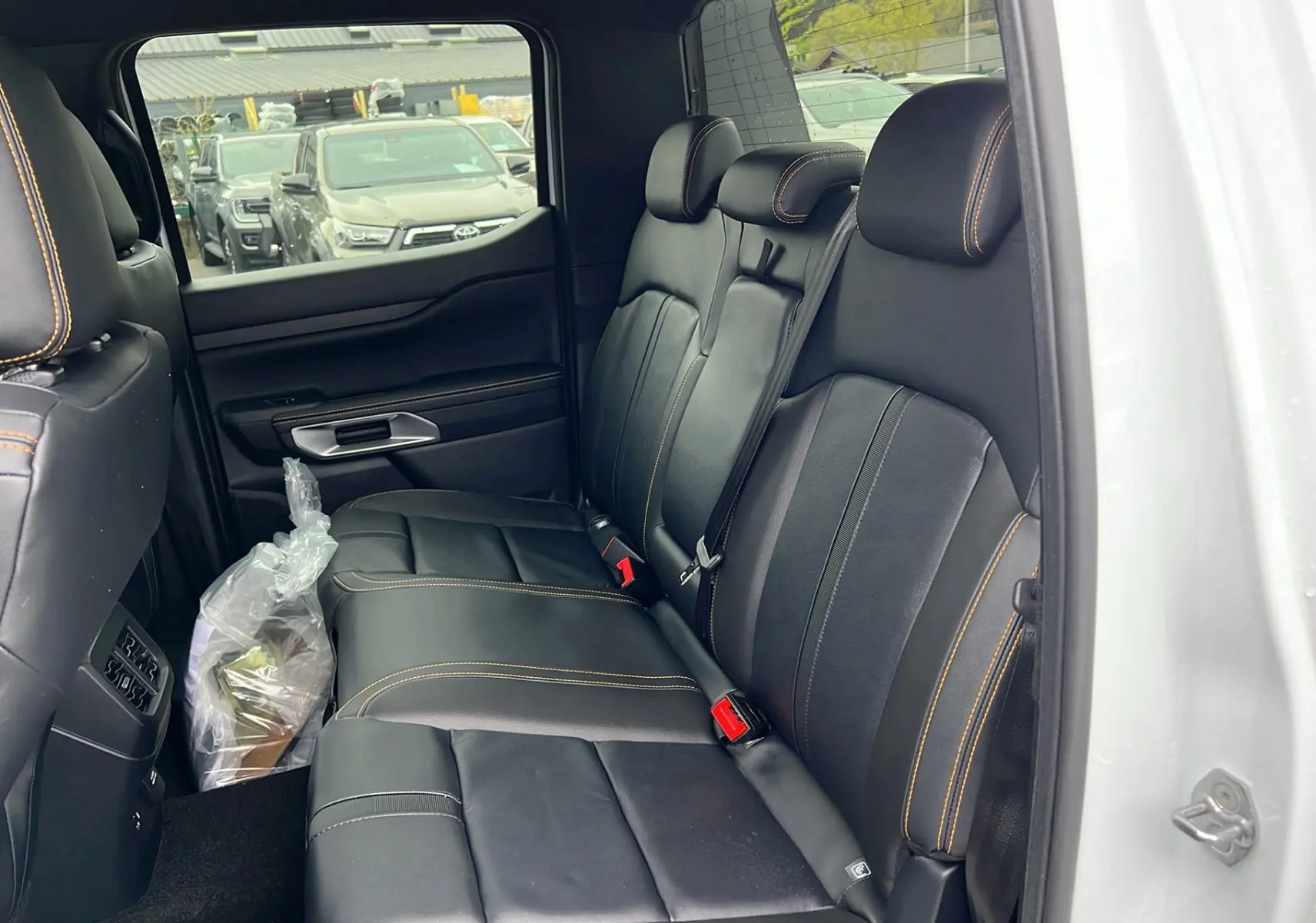 Vue intérieure côté droit sur la banquette arrière en cuir noir avec surpiqûres orange du Ford Ranger blanc glacier 2025.