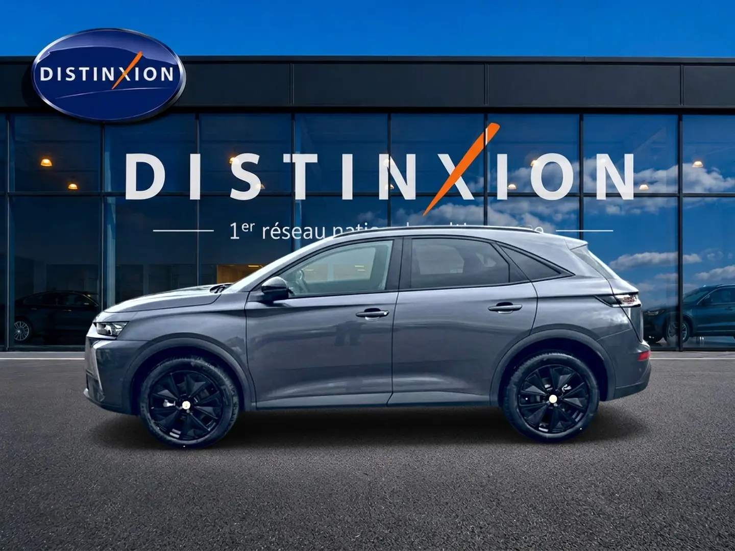 Vue latérale droite d'un DS7 gris titane avec jantes noires, garé devant une vitrine Distinxion.