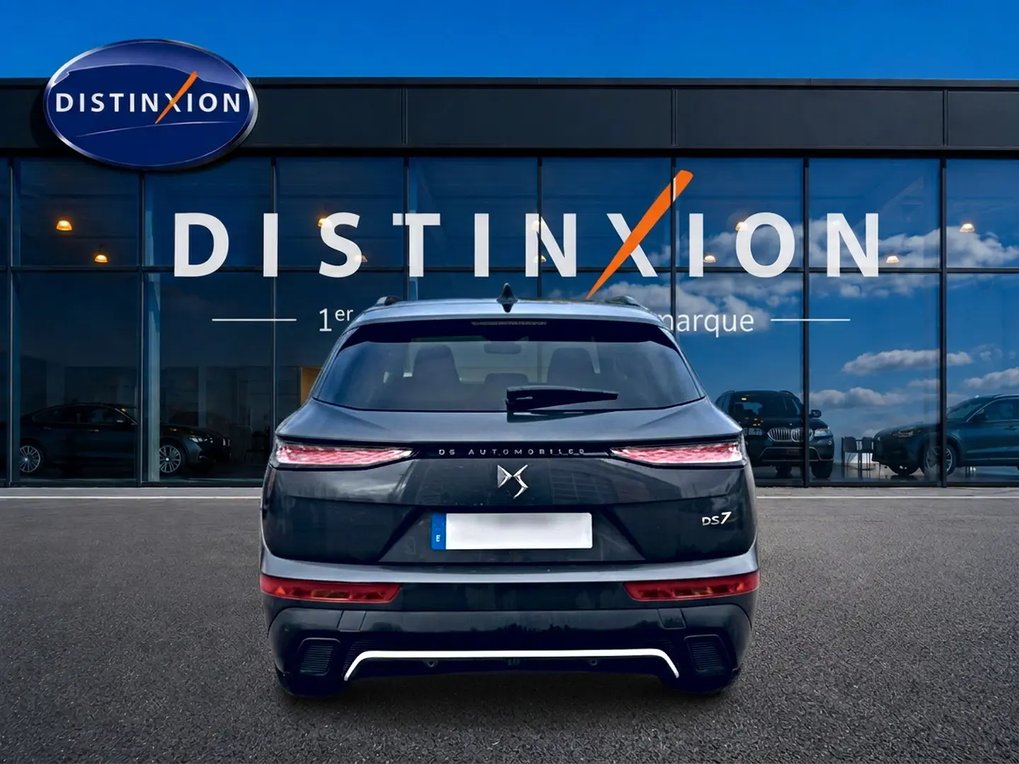 Vue arrière d'un DS7 gris titane 2026 avec feux LED fins et double sortie d'échappement, devant une vitrine Distinxion.