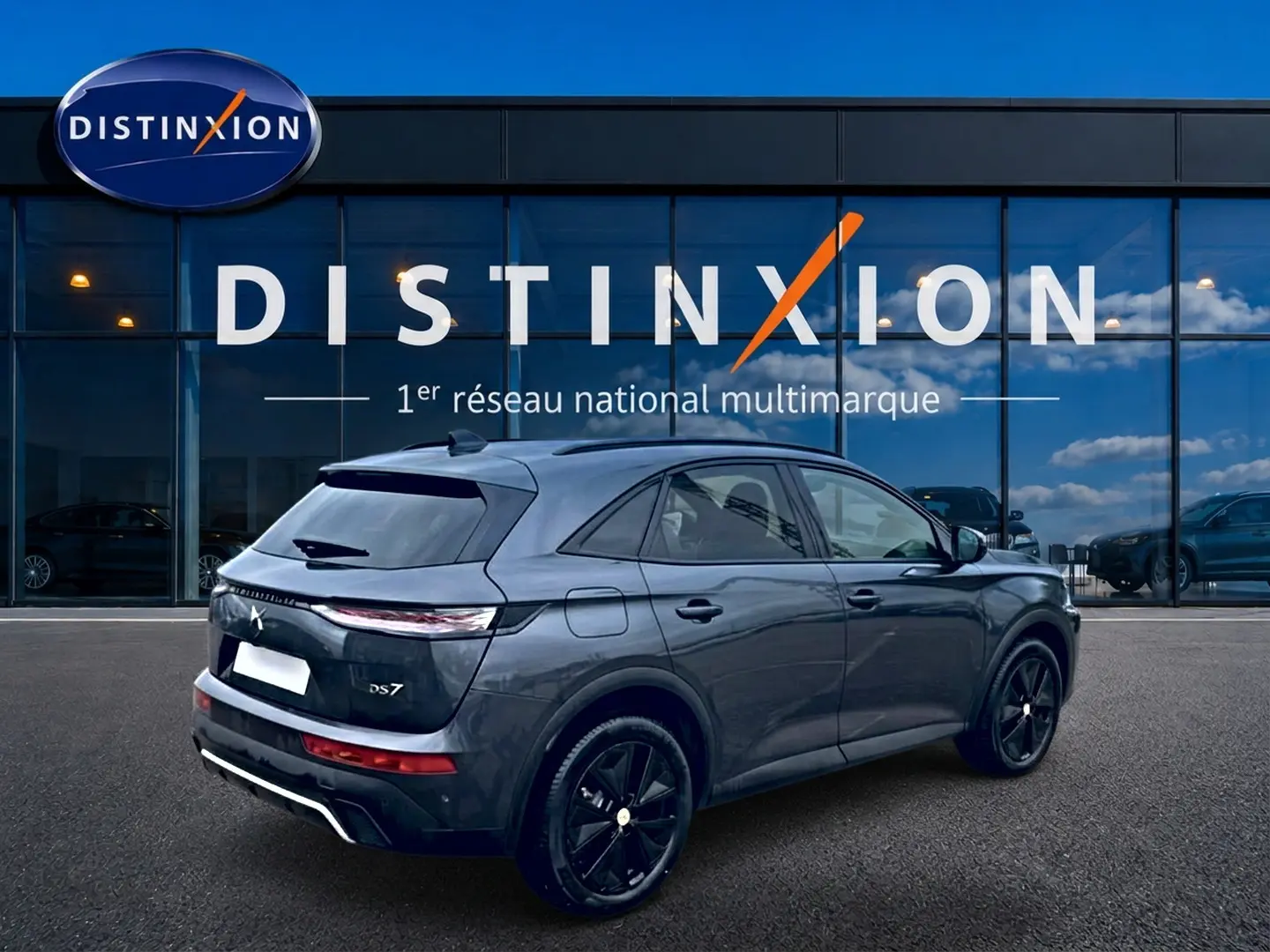 Vue 3/4 arrière droite du DS7 gris titane avec jantes noires devant une vitrine Distinxion.