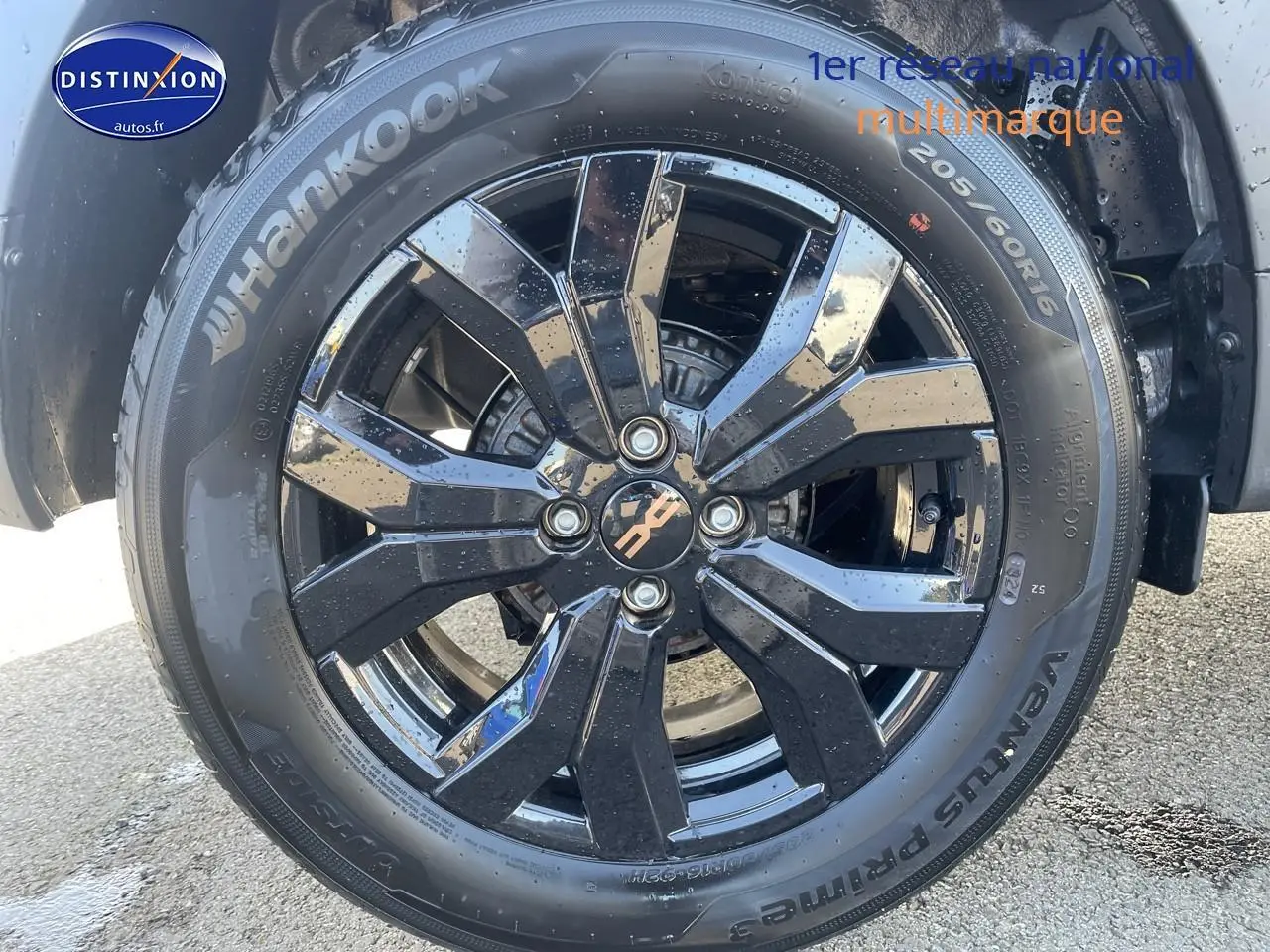 Gros plan sur la jante alu noire brillante d'une Dacia Sandero Stepway gris schiste avec pneu Hankook humide.