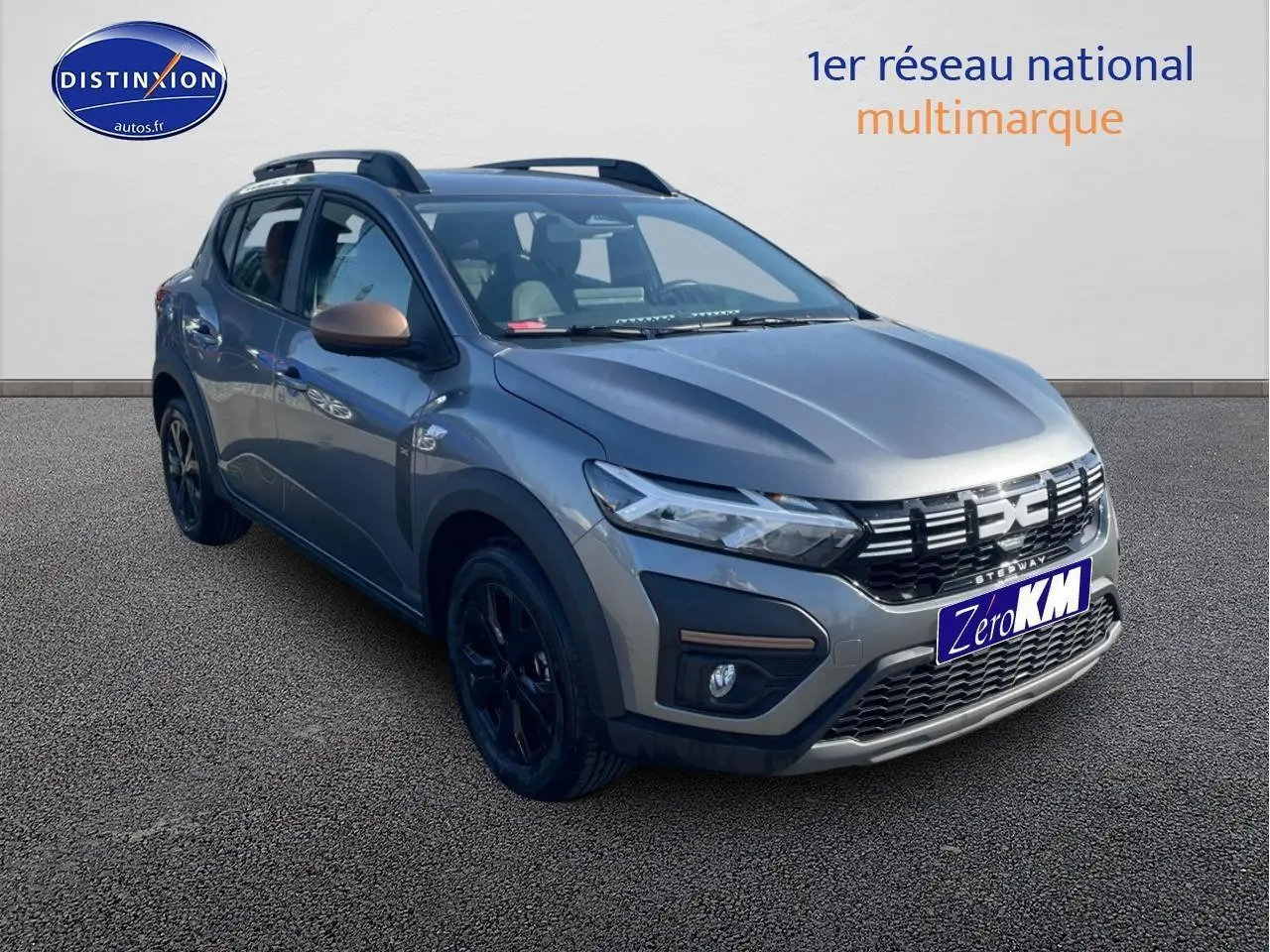 Dacia Sandero Stepway gris schiste vue 3/4 avant droit avec barres de toit et jantes noires.