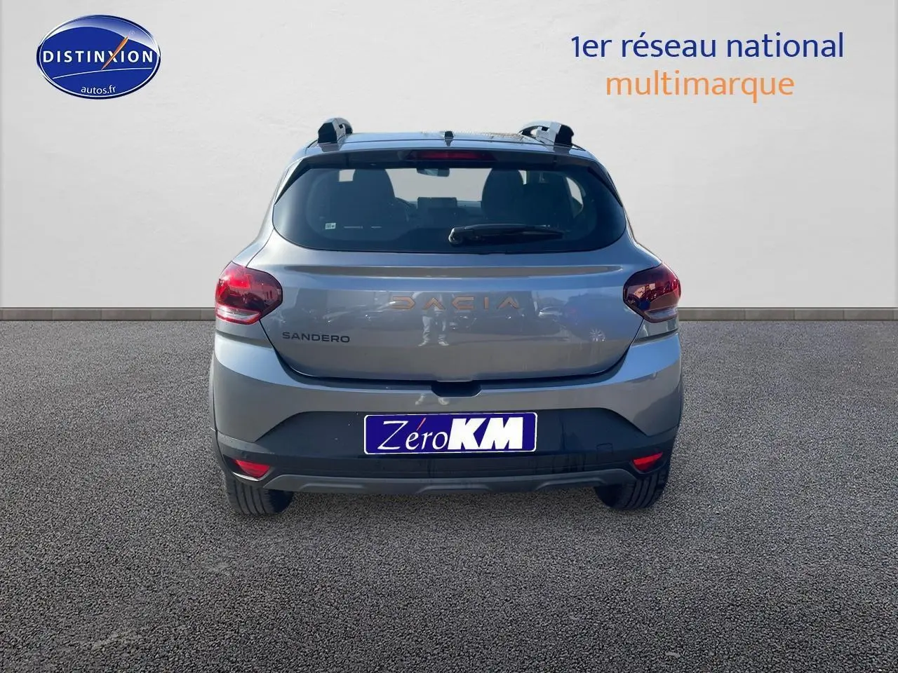 Vue arrière d'une Dacia Sandero gris schiste 2025 avec barres de toit et feux arrière rouges.