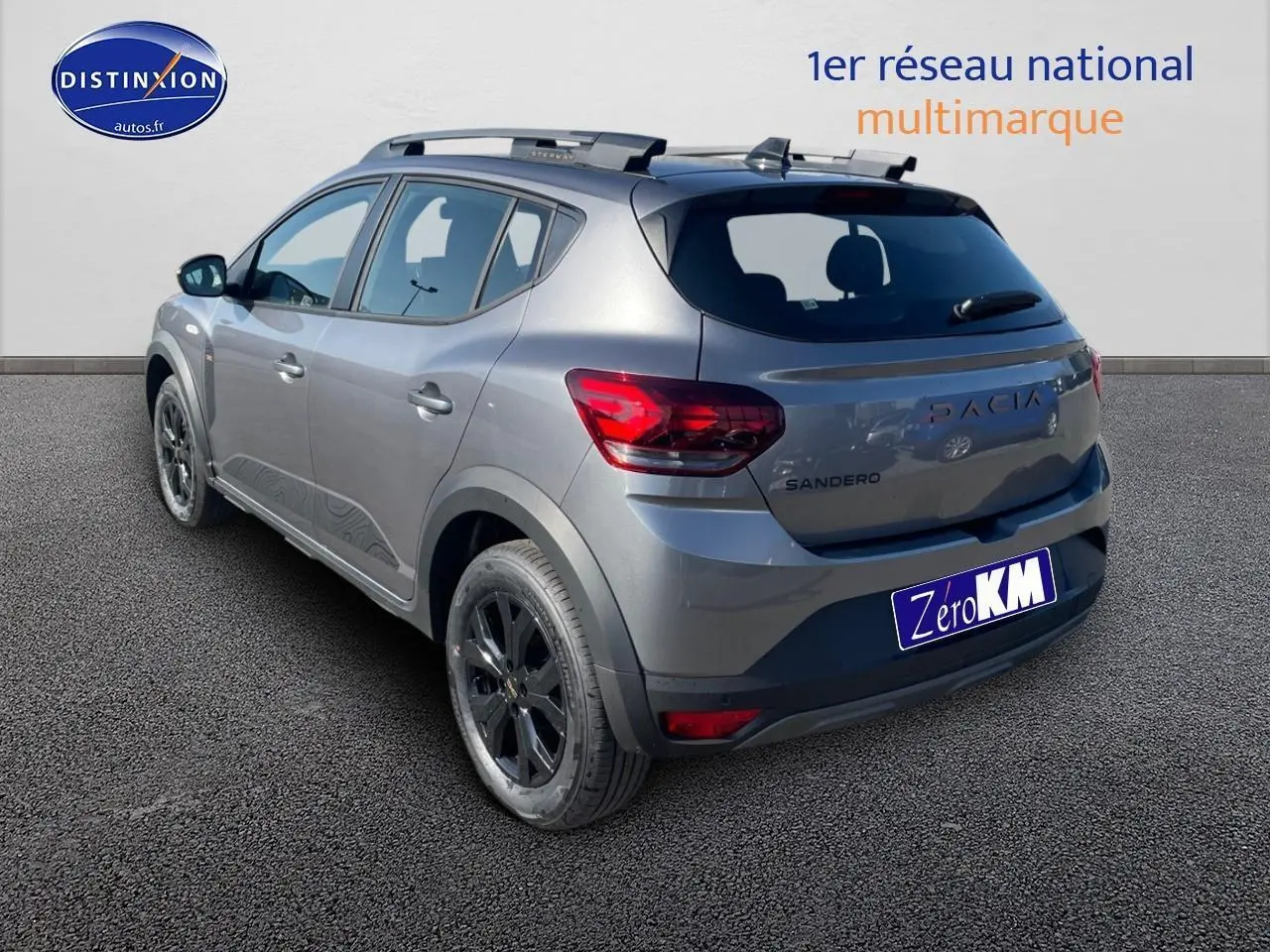 Vue 3/4 arrière droite d'une Dacia Sandero gris schiste avec barres de toit et jantes alu noires.