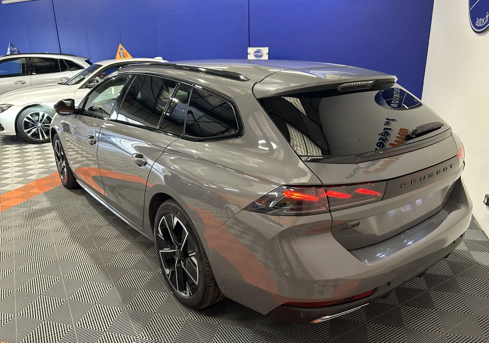 Peugeot 508 SW gris Selenium vue 3/4 arrière droit, feux LED allumés et vitres teintées dans un showroom.